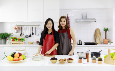 Smiling ethnic females in aprons serving fresh ripe fruits on table in kitchen