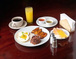 Latin breakfast with all kinds of ingredients like bananas, beans, eggs. coffee and juice to drink
