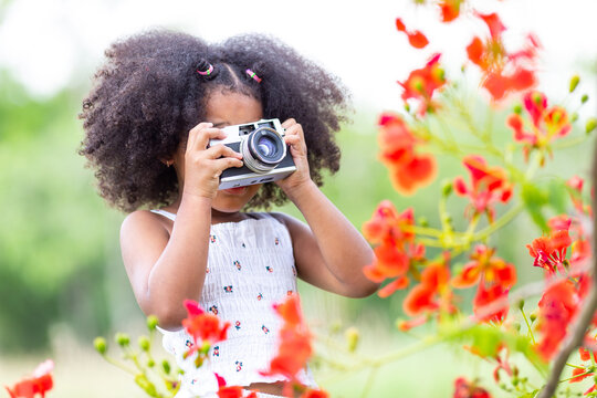 Childhood and explorer concept - A small curly haired African American girl holding a flower camera.