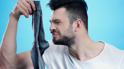 grimacing man smelling stinky sock isolated on blue
