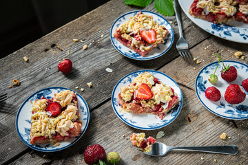 Strawberry and rhubarb meringue crumble squares on white and blue plates on wooden table.