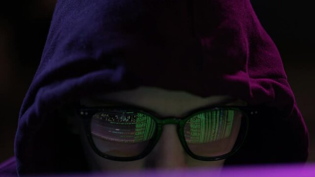 Portrait of female software developer wearing eyeglasses, working on computer, projected code numbers and characters. Green binary hacking code reflecting in eyeglasses in dark room.