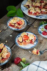 Strawberry and rhubarb meringue crumble squares on white and blue plates on wooden table.