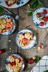 Strawberry and rhubarb meringue crumble squares on white and blue plates on wooden table.