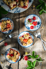 Strawberry and rhubarb meringue crumble pie on white and blue plates on wooden table.