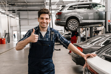 Young car mechanic smiling and showing thumb up while standing in garage