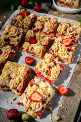 Strawberry and rhubarb meringue crumble squares on baking paper on old wooden table.