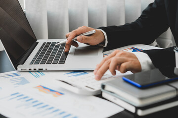 businessman or accountant hand holding pen working on calculator and laptop computer to calculate business data during make note at notepad, accountancy document at office