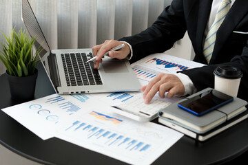 businessman or accountant hand holding pen working on calculator and laptop computer to calculate business data during make note at notepad, accountancy document at office