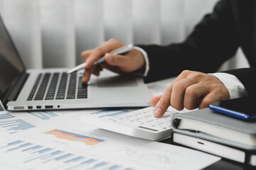 businessman or accountant hand holding pen working on calculator and laptop computer to calculate business data during make note at notepad, accountancy document at office