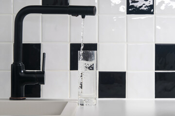 tap water is poured into a transparent glass, against a background of black and white tiles