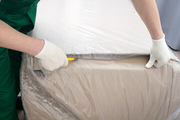the delivery man's hands in protective gloves, opens the furniture from the box, cuts through the dense polyethylene