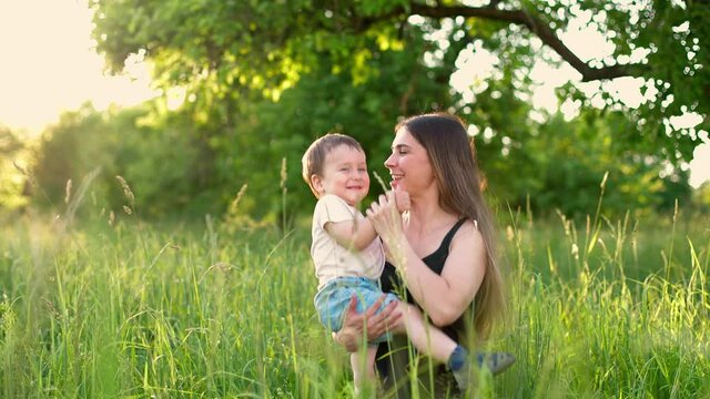 Happy mother hugs and whirls with her little son in park. Young mom and her baby son in a green park having fun. Happy smiling people. Slow motion