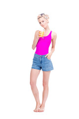 Vertical full length studio portrait of modern young Caucasian woman wearing summer outfit drinking fresh orange juice, white background