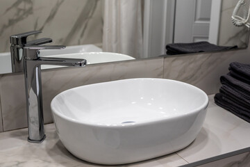 New clean white vessel sink and shiny metal faucet on countertop near large mirror in light...