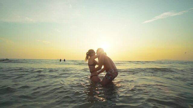 Young happy couple in love having romantic tender moments at sunset in the sea on the tropical beach. Summer vacation amd love concept. Slow motion