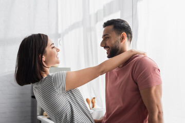 positive young couple looking at each other and hugging in kitchen