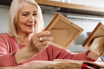 A positive elderly woman looking at old photographs as part of sitting in the kitchen