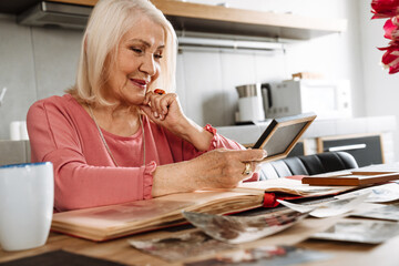 A smiling elderly woman looking at old framed photo sitting in kitchen