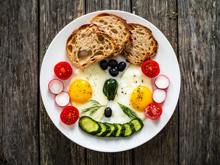 Continental breakfast - sunny side up eggs, bread and  fresh vegetables on wooden table
