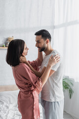 smiling young couple looking at each other and gently touching each other in bedroom