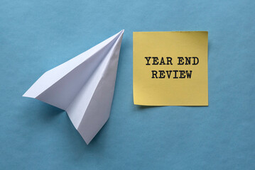 Year end review concept written on yellow memo note with paper plane on blue background.