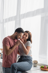 young man with closed eyes kissing hand of girlfriend in kitchen