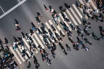 Fotobehang Different people at a pedestrian crossing in the city. People at a zebra pedestrian crossing - a lot of pedestrians in an overcrowded city on a sunny day. Aerial drone shot.  © Andrii Chagovets