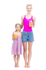 Vertical full length studio portrait of modern Caucasian woman and girl wearing summer clothes standing together drinking fresh orange juice