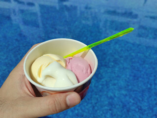 Ice Cream cup in hand on swimming pool background