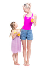 Vertical full length studio portrait of modern Caucasian woman and girl wearing summer clothes standing together drinking fresh orange juice