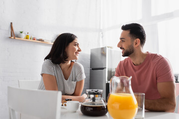 happy young couple sitting at table with breakfast, coffee and orange juice in kitchen