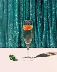A glass of champagne cocktail with some parsley on the bottom in front of green glossy curtain....