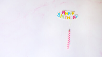 Flat lay of a birthday candle with a paper speech bubble on top, written Happy Birthday in colorful letters. With pink marble background.