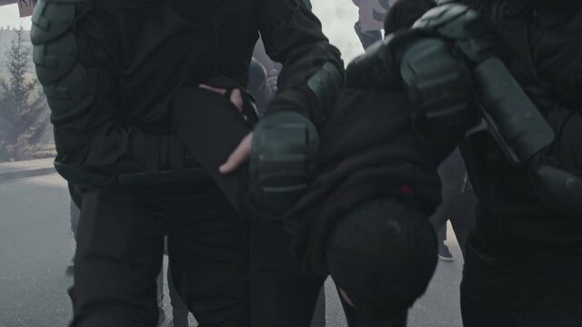 Slowmo tracking shot of riot police officers in full gear confronting protesters with signs and smoke bombs and arresting man