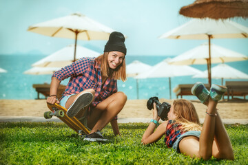 Portrait of beautiful skateboarding woman on skateboard and girl making photos at summer green park