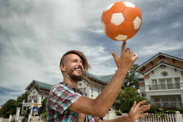 Young man playing with a football ball. Atractive man spinning a ball on his finger on the street
