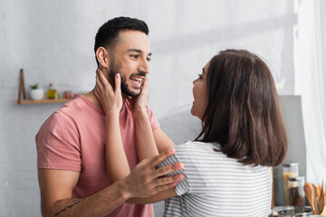 smiling young couple hugging and touching each other with hands in modern kitchen