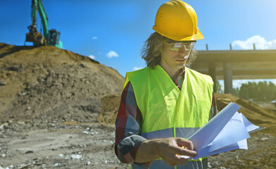 Builder with documents on the background of a road junction construction site.