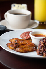 Latin breakfast with fried plantain, scrambled eggs, ground beans, chorizo ​​and orange juice or coffee, all on a white plate
