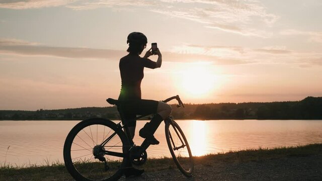Woman cyclist taking photos of beautiful sunset. Cycling at sunrise. Triathlon motivation