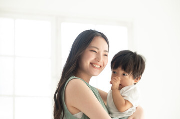 赤ちゃんを白い綺麗な部屋で抱っこする笑顔の美人ママ4 　ズームコピースペースあり
