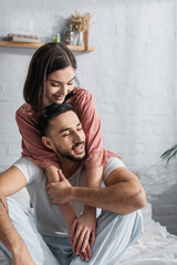 happy young couple sitting on bed with white linen and hugging in bedroom