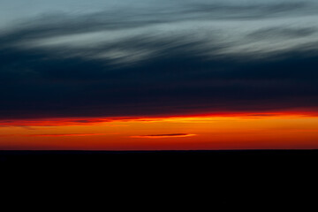 Dawn sunrise sunset is located in a stripe in a field on the horizon, the natural background of a beautiful bright colorful dramatic sky with clouds in red-yellow orange tones