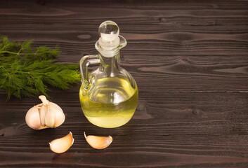 Garlic oil in a glass decanter on a wooden table, garlic next to it. Free space for text.