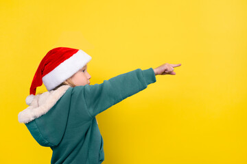 Fototapeta na wymiar Little beautiful girl in santa hat smiling and pointing her finger. Banner with copy space. Christmas concept