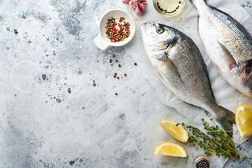 Raw dorado fresh fish or sea bream with ingredients for making lemon, thyme, garlic, cherry tomato and salt on light grey slate, stone or concrete background. Top view with copy space.