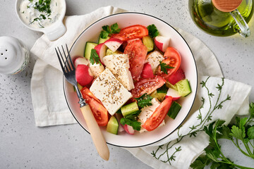 Radish, cucumber, tomato, pepper and feta cheese with spices pepper and olive oil in white bowl on grey slate, stone or concrete background. Healthy food concept. Top view.