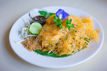Fried rice noodles with prawns in a thin omelet wrapping is served with fresh bean spouts and lemon.  It’s a Thai street food style.