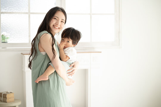 赤ちゃんを白い綺麗な部屋で抱っこする笑顔の美人ママ3 カメラ目線コピースペースあり